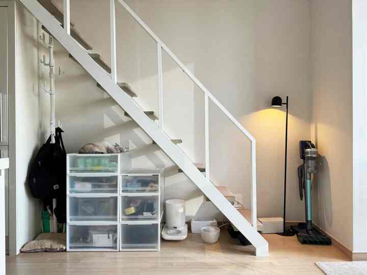 白とナチュラルカラーのロフト階段スペース、透明な収納ケースとコートラックが配置された温かみのあるインテリア