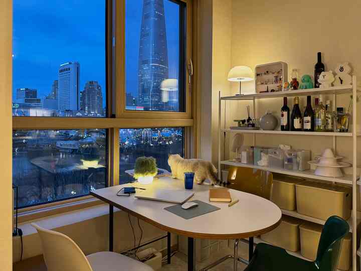 白とベージュの色調のダイニングルーム、テーブルの上に猫が座り、壁の棚と窓からの夜景が調和した落ち着いた空間