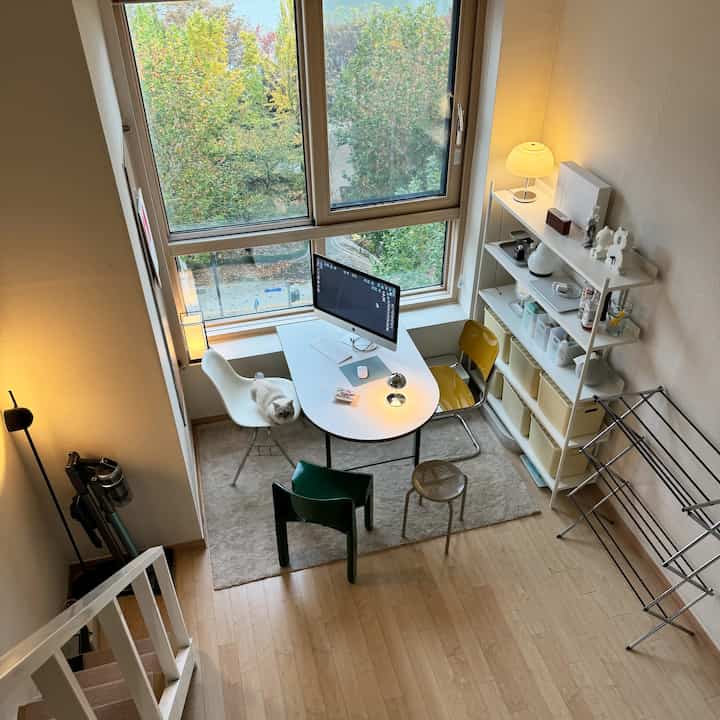 明るいホワイトとウッドトーンが調和した一人暮らし用ホームオフィス、広い窓と実用的な家具配置で快適な空間