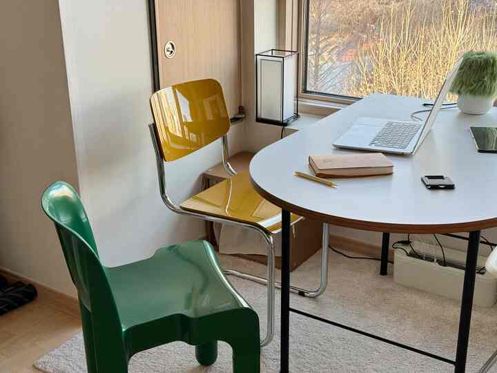 ミッドセンチュリーモダン風のコンパクトな作業空間、白いダイニングテーブルと黄色と緑の椅子が配置された清潔な室内