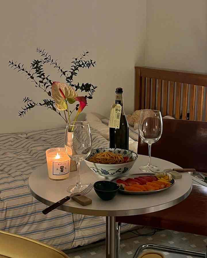 白と木目調のキッチン空間、円形のダイニングテーブルにキャンドルとワイングラス、食事が置かれた雰囲気のあるミッドセンチュリーモダンインテリア