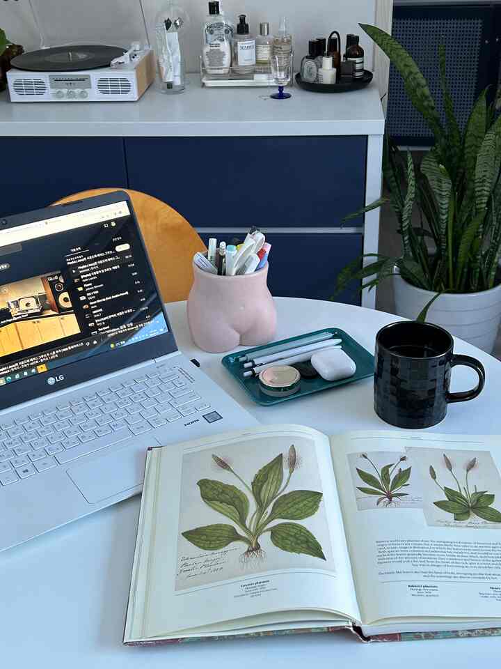 白とシルバーのトーンのワンルームホームオフィス、丸テーブルにノートパソコンと植物、コーヒーマグが配置されたすっきりとした作業空間