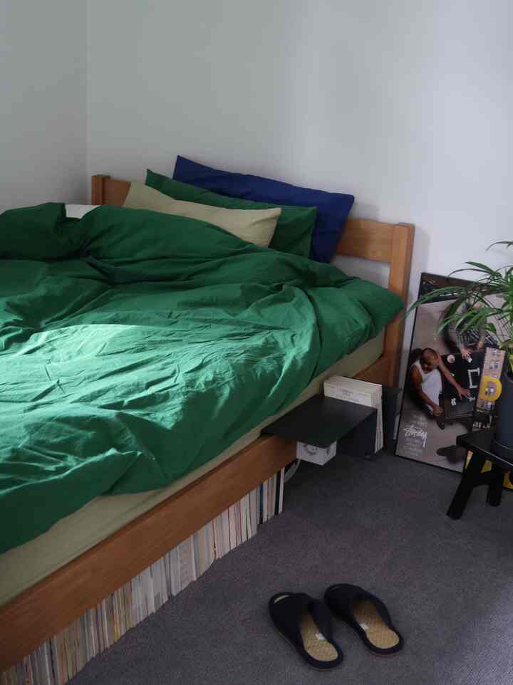 ネイビーとグリーン調の寝室、木目調ベッドフレームと緑の寝具が配置された雰囲気のある空間