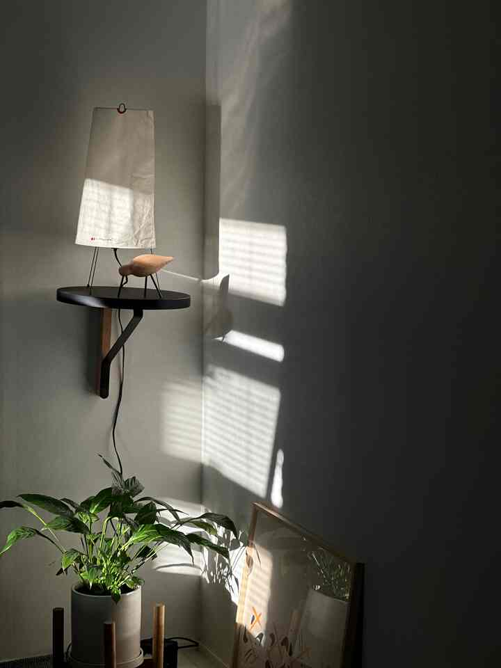 白とナチュラルな色調の書斎の一角、フロアランプと植物、額縁が配置されたシンプルで落ち着いた空間