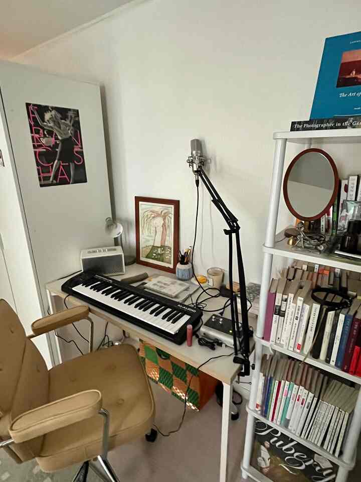 白い壁とベージュのアームチェア、MIDIキーボードとマイクブームアームがある在宅勤務用のホームオフィススペース