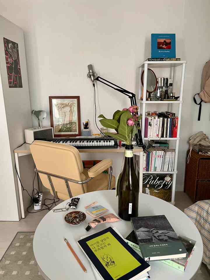 ベージュ色のオフィスチェアと丸テーブルが配置された、書籍と音楽機器のあるワンルームのホームオフィス空間