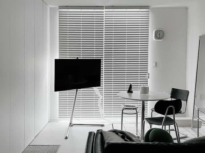 白と黒のモノトーンのリビング、ブラインドとステンレス素材のダイニングテーブルや椅子が配置されたミッドセンチュリーモダンなインテリア