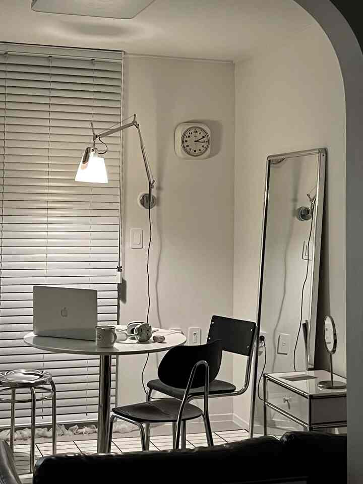 モノトーンでシンプルなホームオフィス、丸いダイニングテーブルとスツール、ブラインドが配置された落ち着いた雰囲気のインテリア