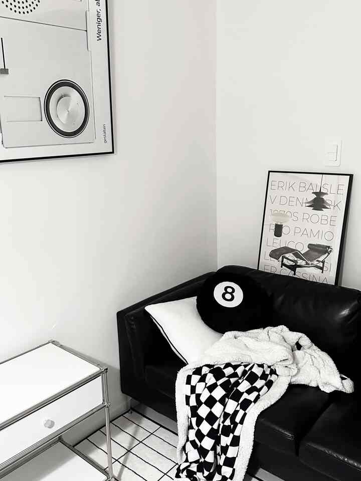 黒と白のトーンのリビングコーナー、黒革のソファ、白いサイドテーブル、額装された壁飾りが配置されたミッドセンチュリーモダンの空間