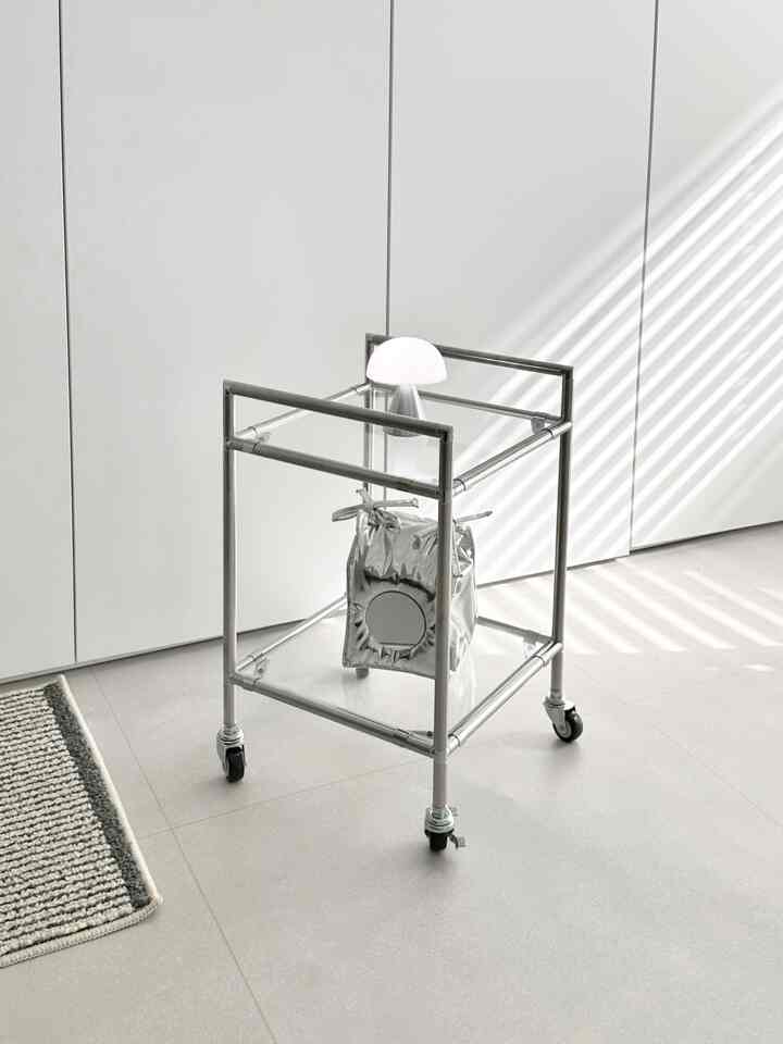 シルバーフレームと透明ガラスのモジュール式金属製トロリーが配置され、上部には白いLEDキノコランプがあるモダンで清潔感のある空間。