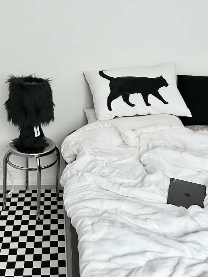 白と黒のトーンが特徴的なモダンな寝室、ダブルベッドとスツールの上にあるファーランプが配置されている