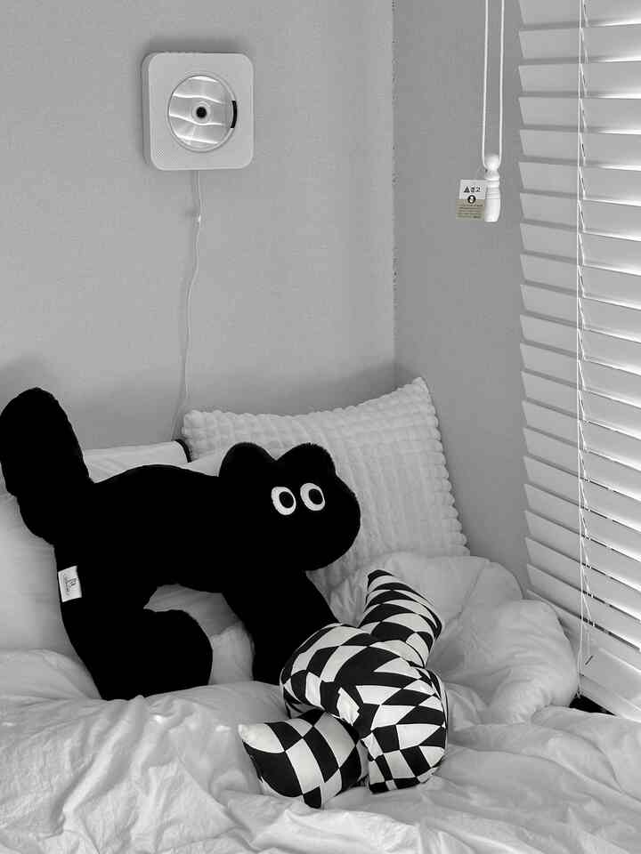 ホワイトとブラックのモノトーンの寝室、黒い猫のぬいぐるみとチェック柄クッションが配置された雰囲気のある空間