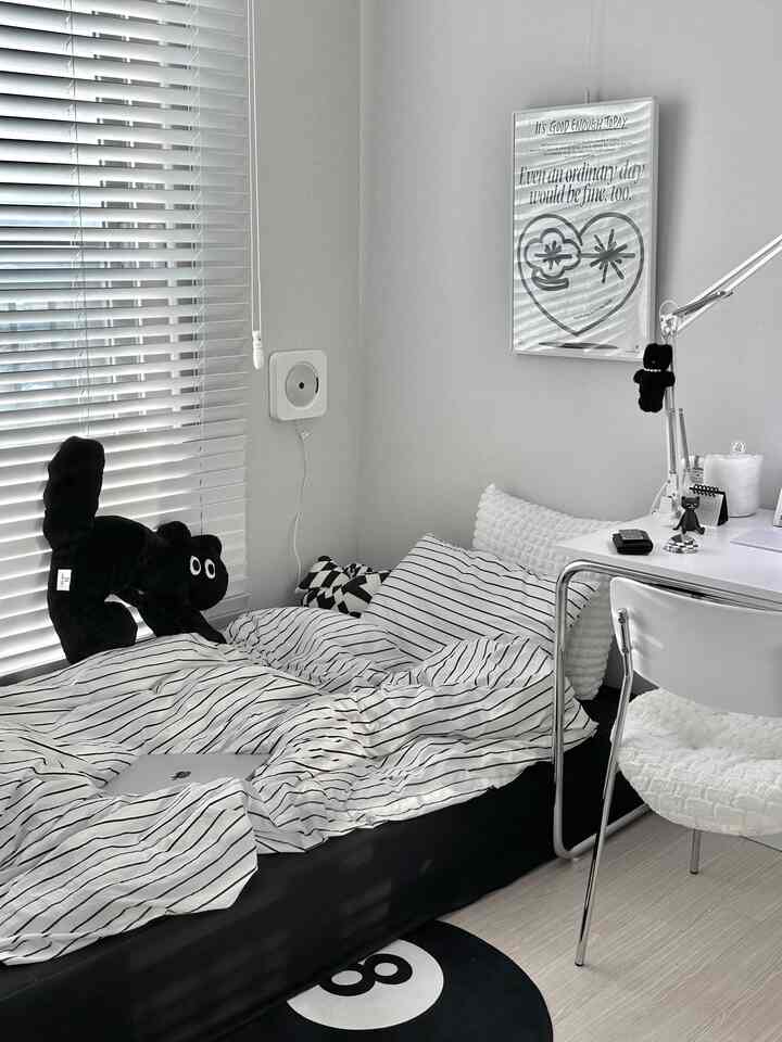 白と黒のトーンが基調のコンパクトな寝室、ストライプの寝具とデスク、ラグが配置された洗練された空間