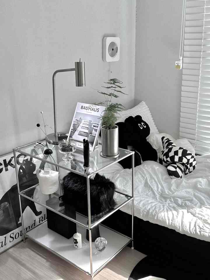 白と黒のトーンのミニマルモダンな寝室、メタル製モジュラーシェルフと枕、ブラインドが配置された清潔感ある空間