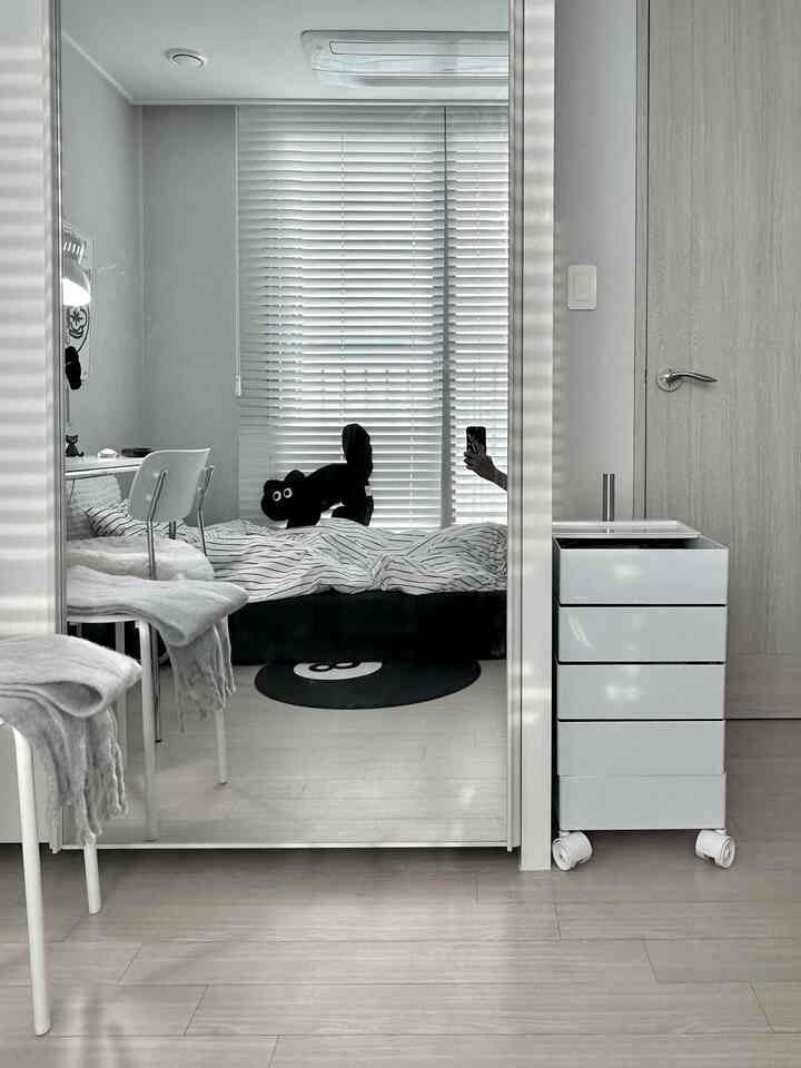 白とナチュラルカラーの寝室、クローゼットの鏡とブラインドが配置された雰囲気のあるミニマルな空間