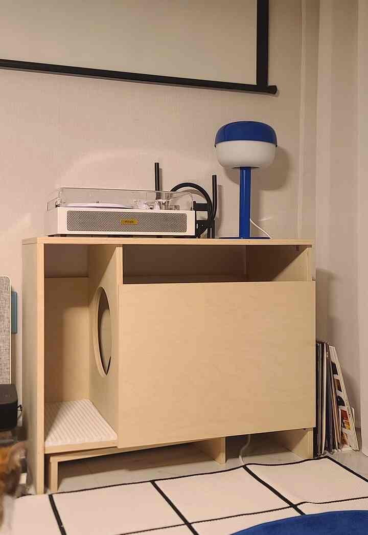 白と木目調のリビング、モダンなインテリアにカスタム猫トイレとターンテーブルが配置された印象的な空間