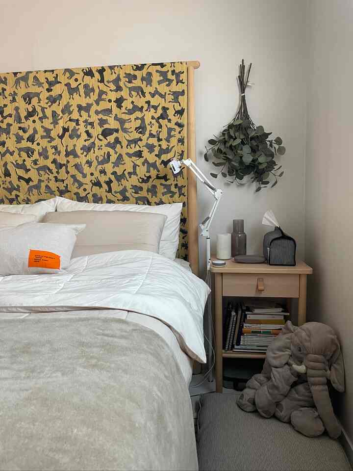 ナチュラルな色調の書斎寝室、猫柄のヘッドボードと木製ナイトテーブル、柔らかい寝具と象のぬいぐるみが配置された印象的な空間