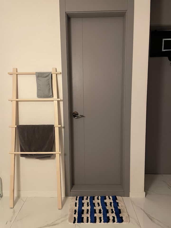 ナチュラルなウッドトーンとブルーが調和するトイレ前の空間、白樺のタオル掛けとパターン入りバスマットが配されたシンプルなインテリア