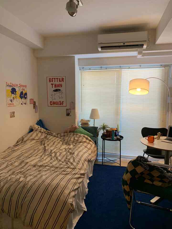 白と青の色調のワンルーム寝室、ベッドとデスク、フロアランプが配置された雰囲気のある空間