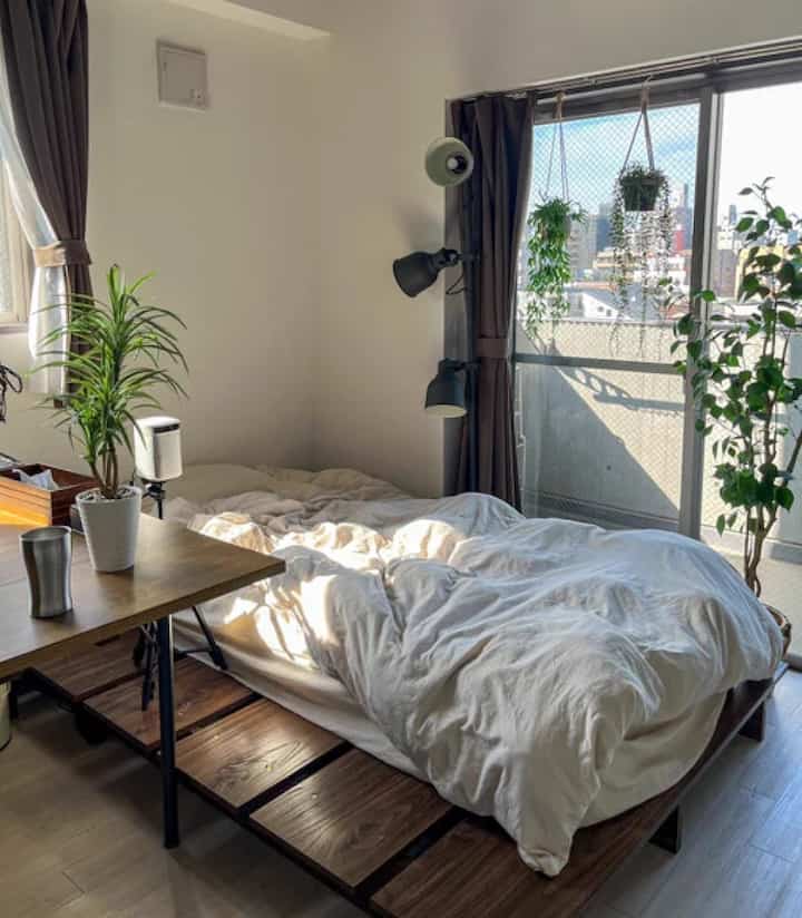 明るい白壁と自然な木目調の寝室、コーナーに設置されたベッドと植物が置かれた雰囲気のあるインテリア