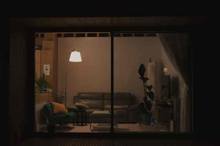 ブラウンの色調のリビング、グレーのソファと緑のアームチェア、フロアランプと植物が配置されたモダンで落ち着いた雰囲気のあるインテリア