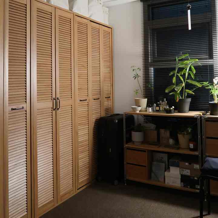 ナチュラルなブラウン調のクローゼットとブラインド、植物が配置された収納中心の小さな部屋