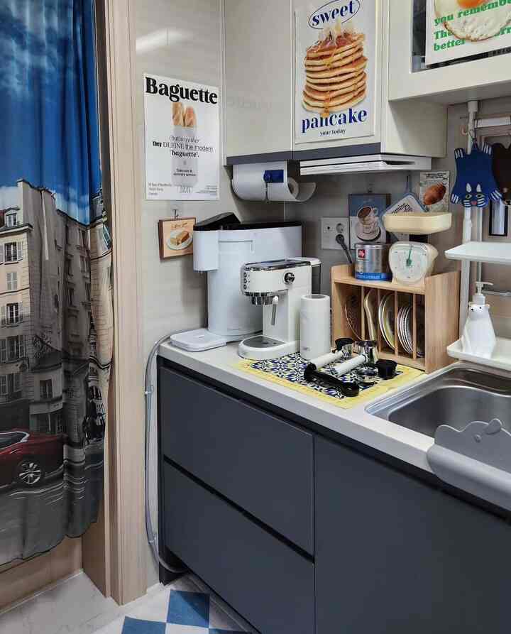 ブルーのカーテンとホワイトキャビネットが調和するシンプルなキッチン、コーヒーマシンとヴィンテージのキッチンスケールが配置された空間