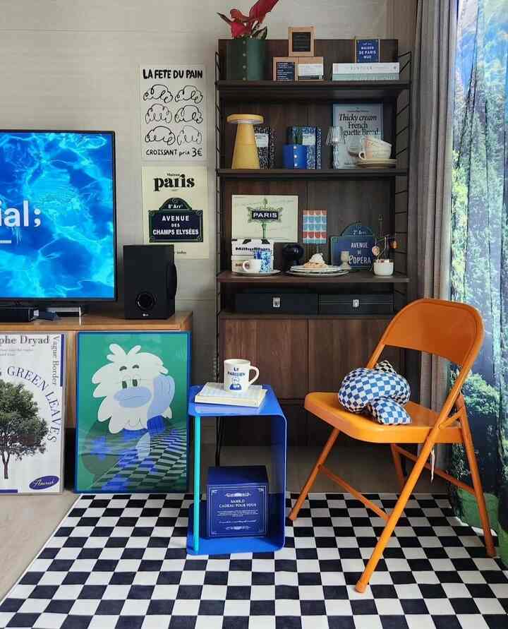 青とオレンジが印象的なリビングコーナー、チェッカーパターンのラグと棚、オレンジ色の折りたたみ椅子が配置されたモダンな空間