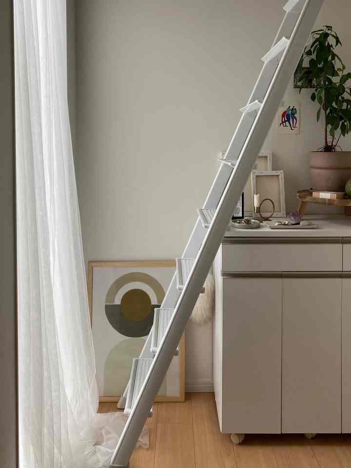 白と木目調のカラーでまとめられたコンパクトなリビングルーム、シンプルな収納キャビネットとはしご、植物が配された雰囲気のあるインテリア