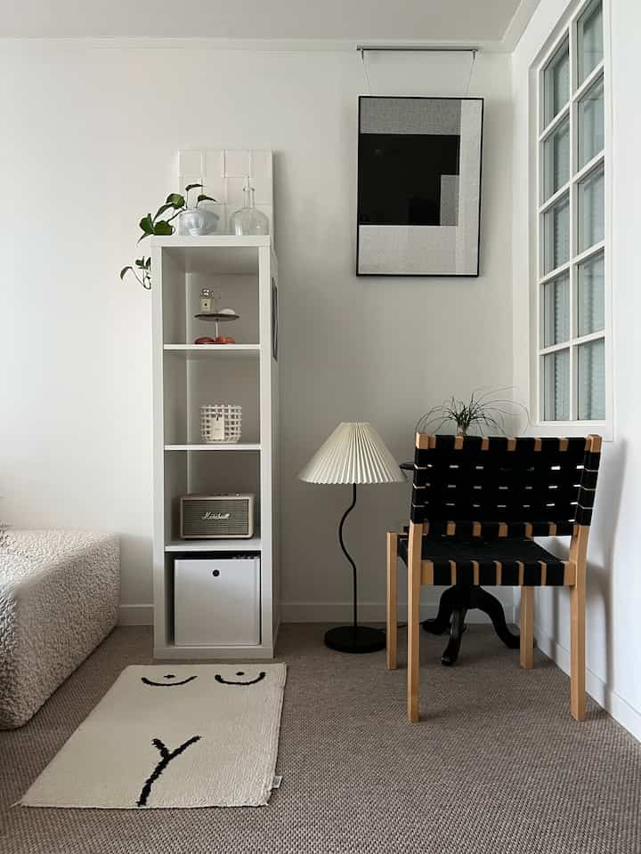 白と黒のトーンのリビング、シンプルな椅子とフロアランプ、整然とした本棚が配置されたミニマルな空間