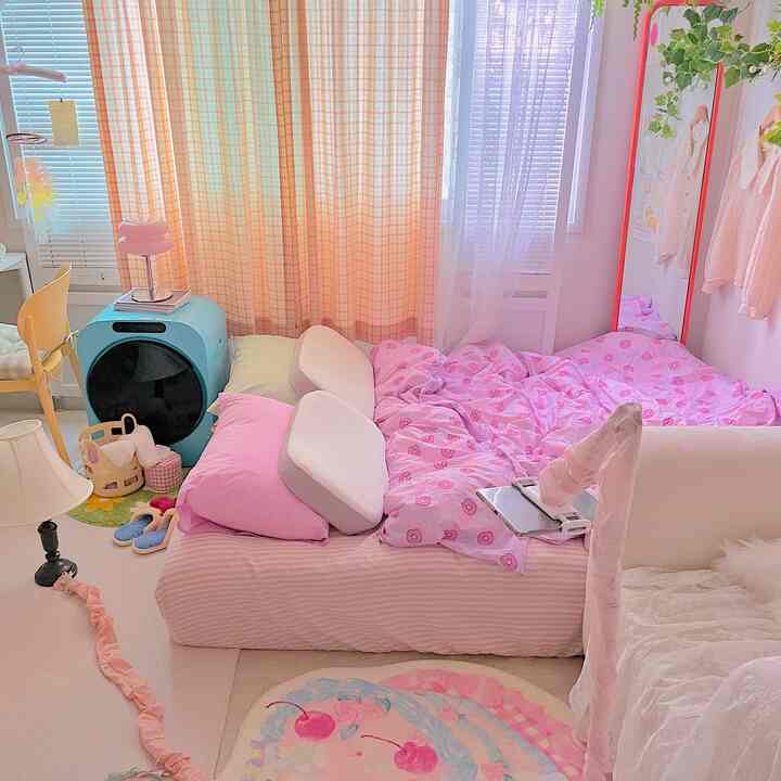 ピンクとホワイト調の寝室、中央にベッドと多様なファブリックが配置された温かみのある空間