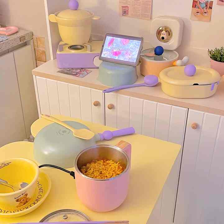 パステルカラーのイエロー調理器具とピンクの電気ポットが置かれたキッチン、整然とした白いキャビネットが配された雰囲気のある空間