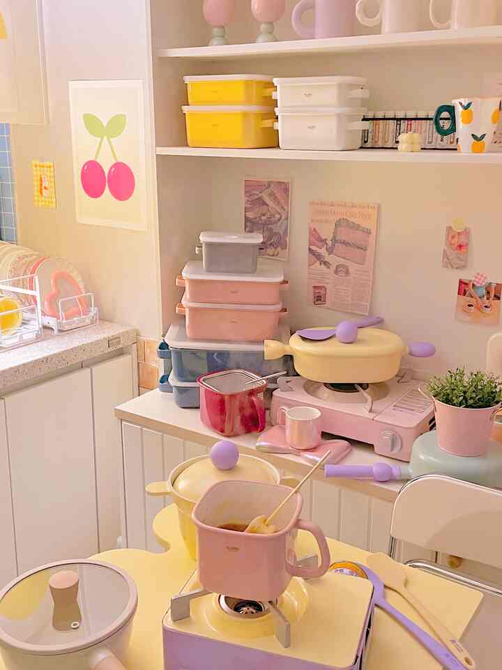 ピンクと黄色のトーンが映えるかわいいキッチン、ポスターとカラフルな調理器具が配置された雰囲気のあるインテリア