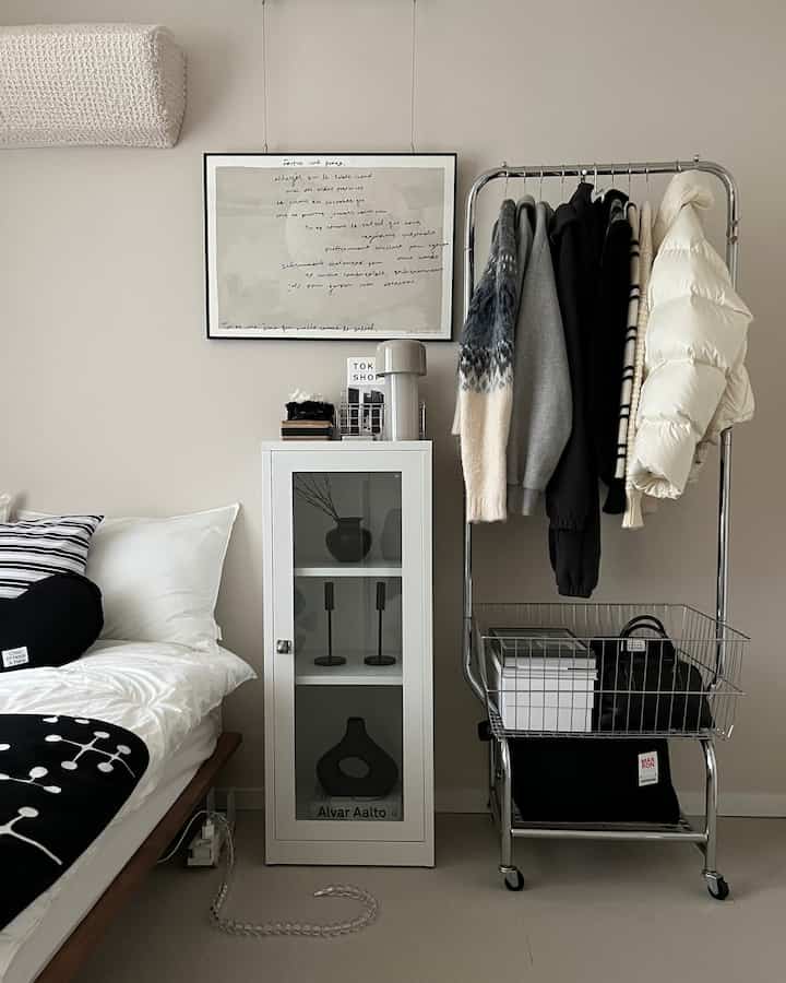 白とモノトーンの寝室、右側にミニクローゼットラック、中央には収納キャビネットが配置されたシンプルモダンな空間