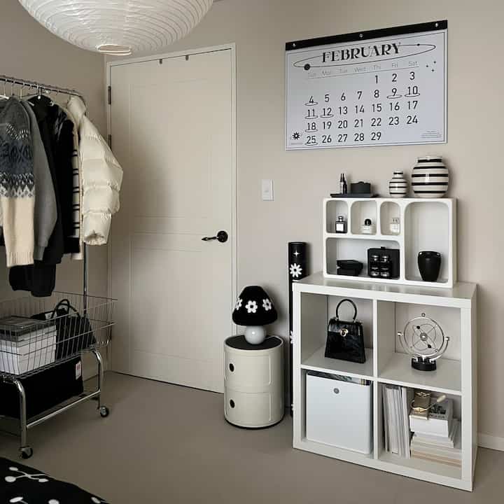 白と黒を基調とした2人暮らし向けの部屋、整頓された本棚とハンガーラック、壁に大きなカレンダーがある雰囲気のあるモダンなインテリア