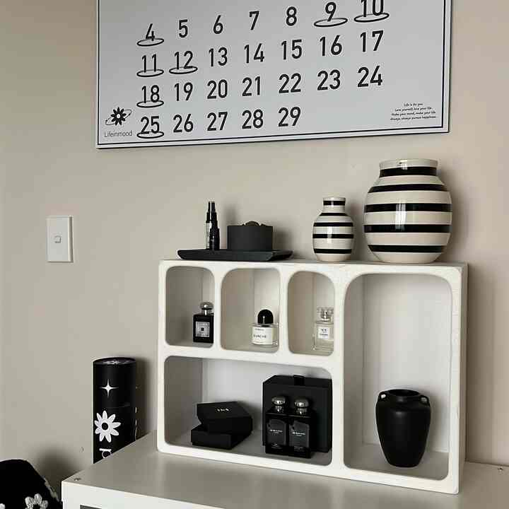 ミニマルでナチュラルな色調の壁面インテリア、白い棚に黒と白のストライプ柄の花瓶や装飾品が配置された空間