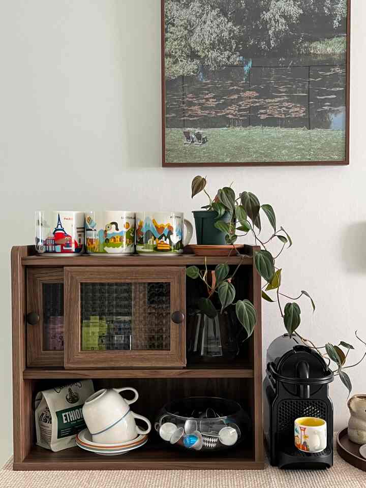 木目調の収納棚にカプセルコーヒーマシン、植物、コーヒーカップが配置されたおうちカフェスペース