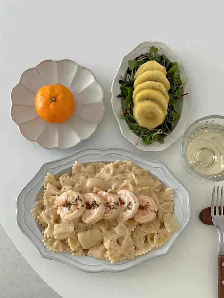 ナチュラルな色調のダイニングテーブルにエビのクリームパスタとキウイサラダ、みかんがきれいに並べられた清潔感のあるおうちカフェの雰囲気