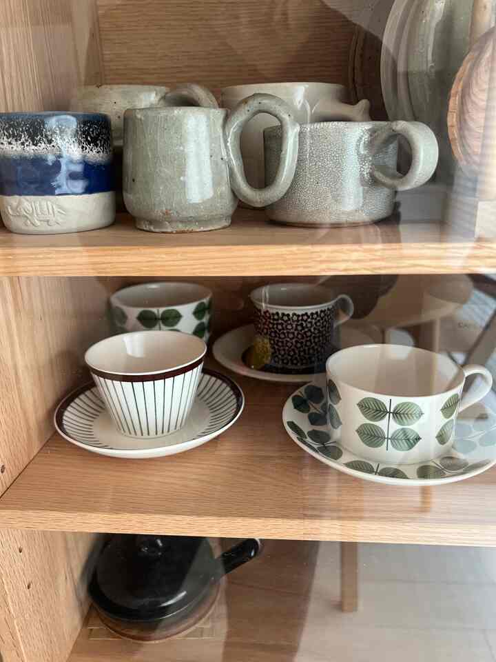 木目調のキャビネットにシンプルで陶器の質感が際立つ北欧ヴィンテージのカップと皿が並ぶ雰囲気のあるインテリア