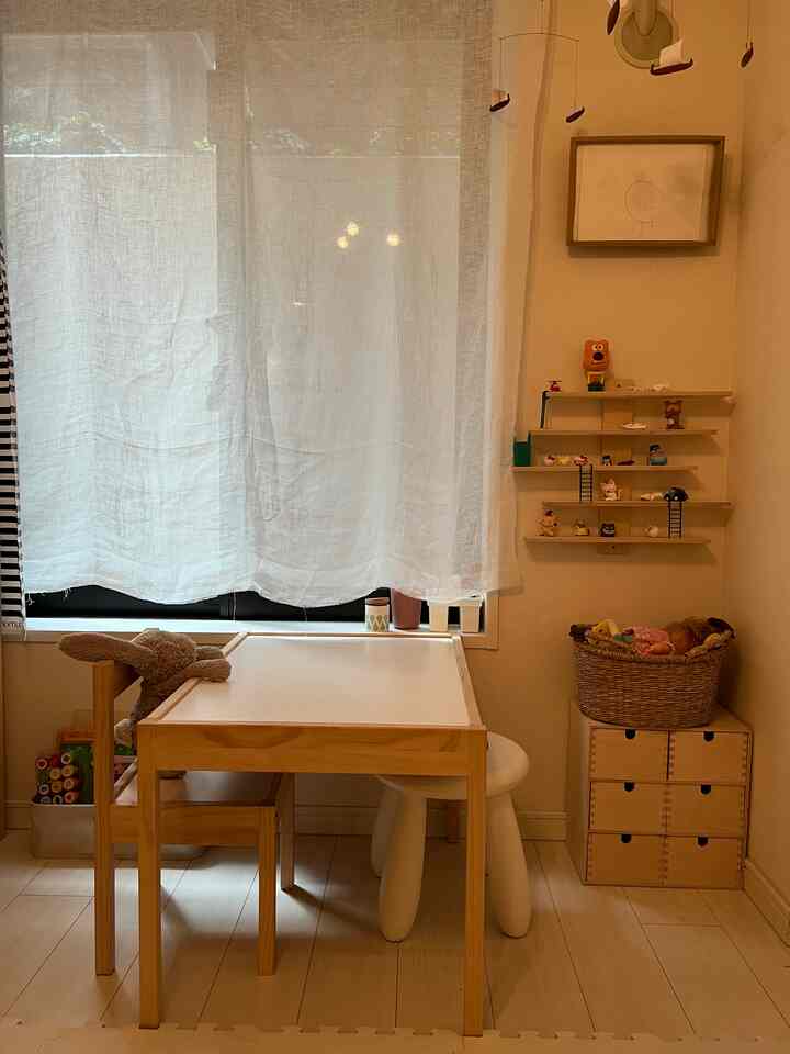 ホワイトカーテンとナチュラルウッド家具が配置された子供部屋、子供用デスクと収納がある温かみのある空間