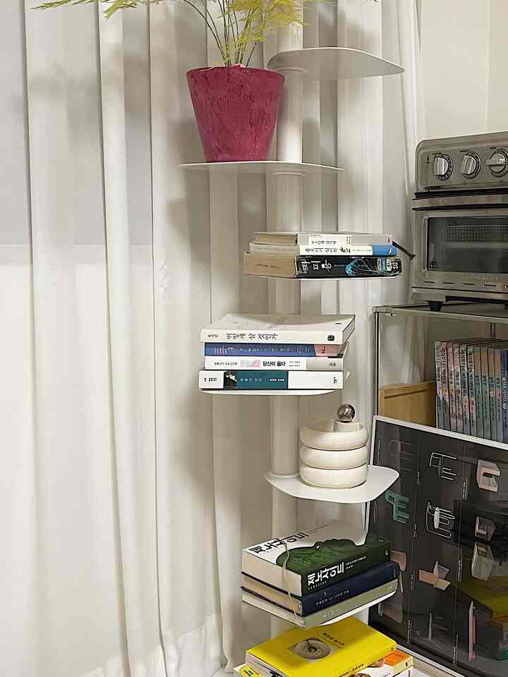 ホワイトを基調とした狭い部屋、白い棚と本棚に本とピンクの鉢植えなどが整然と配置された雰囲気のあるインテリア