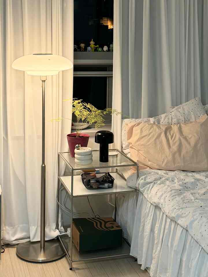 明るいホワイトとベージュトーンの寝室、金属フレームのナイトテーブルとモダンなフロアランプが調和する落ち着いた空間