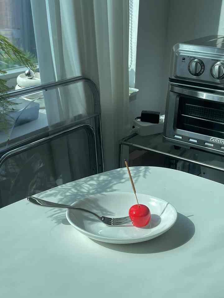 日差しが差し込む白いキッチン空間、中央に皿と赤いトマトのオブジェが配置された印象的なインテリア