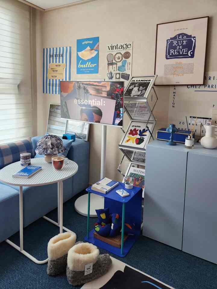 柔らかなブルートーンの寝室コーナー、ソファやサイドテーブル、ヴィンテージスタイルのポスターが配置された雰囲気のあるインテリア