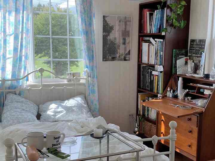 明るいホワイトと木目調の調和が取れた寝室、大きな窓と本棚が配置された雰囲気のある空間