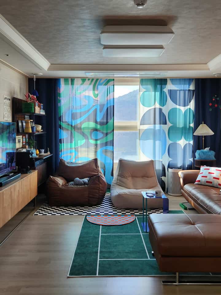 ブルーグリーンの模様カーテンとブラウンレザーソファが配置されたナチュラルモダンのリビング