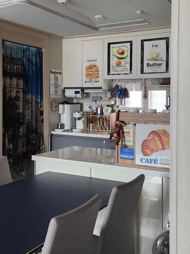 明るく清潔感のある白を基調としたキッチン、前方に広い黒のダイニングテーブルと椅子があり、壁にはヴィンテージ風のポスターが飾られた温かみのある空間