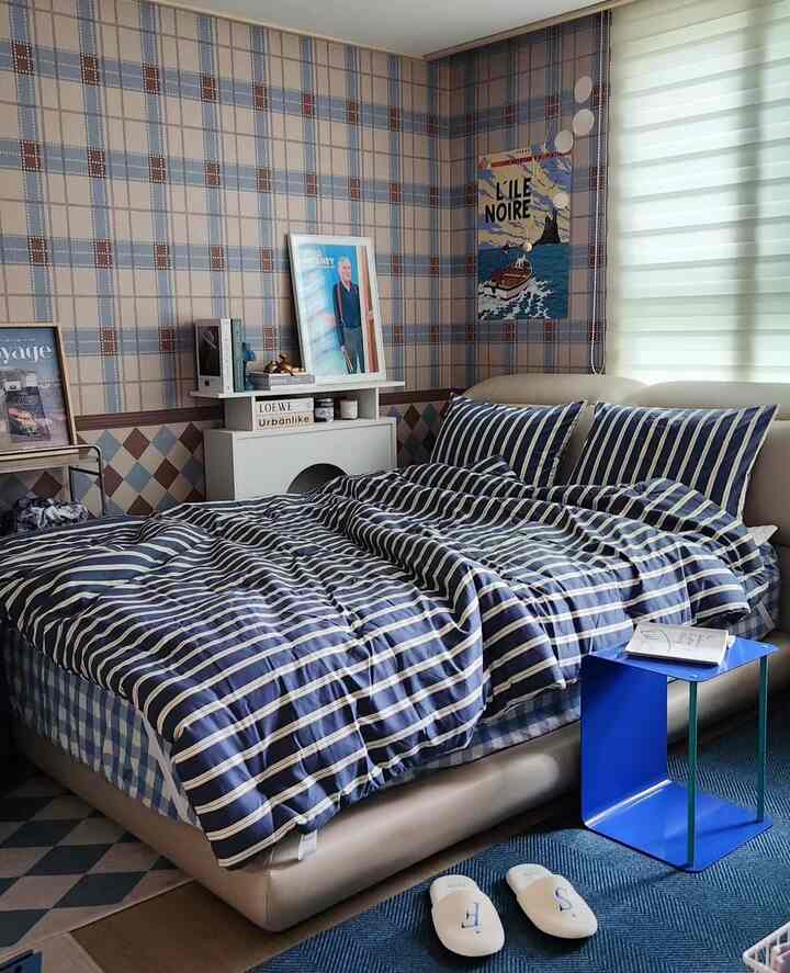 パステルトーンの壁紙と青のストライプ寝具が配置された、落ち着いた雰囲気の寝室