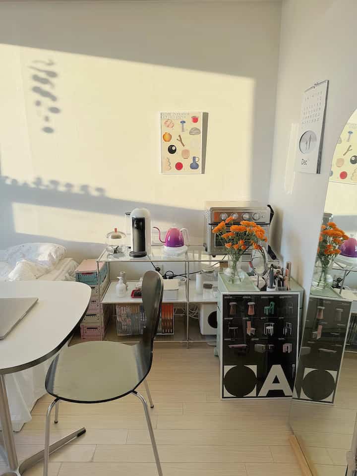 白い壁と木目調の床を持つ小さな寝室、コーヒーマシンとミニオーブンのあるおうちカフェスペースとミニマルな家具配置