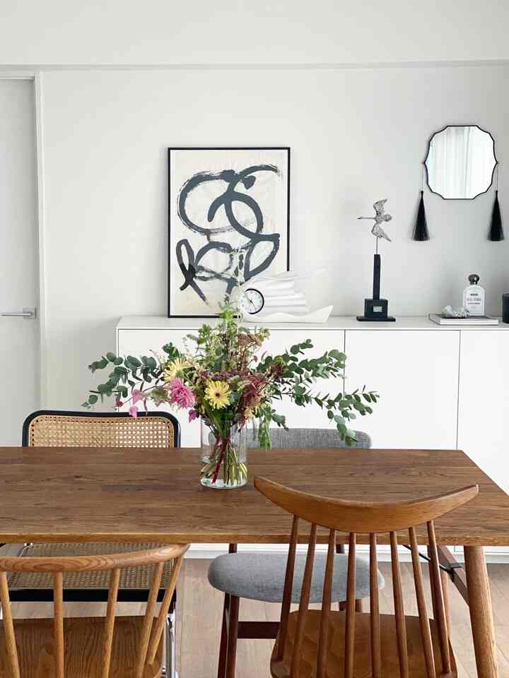 白い壁とナチュラルな茶色のダイニングテーブルが配置されたシンプルなダイニングルーム、中央に花瓶が置かれている印象的な空間